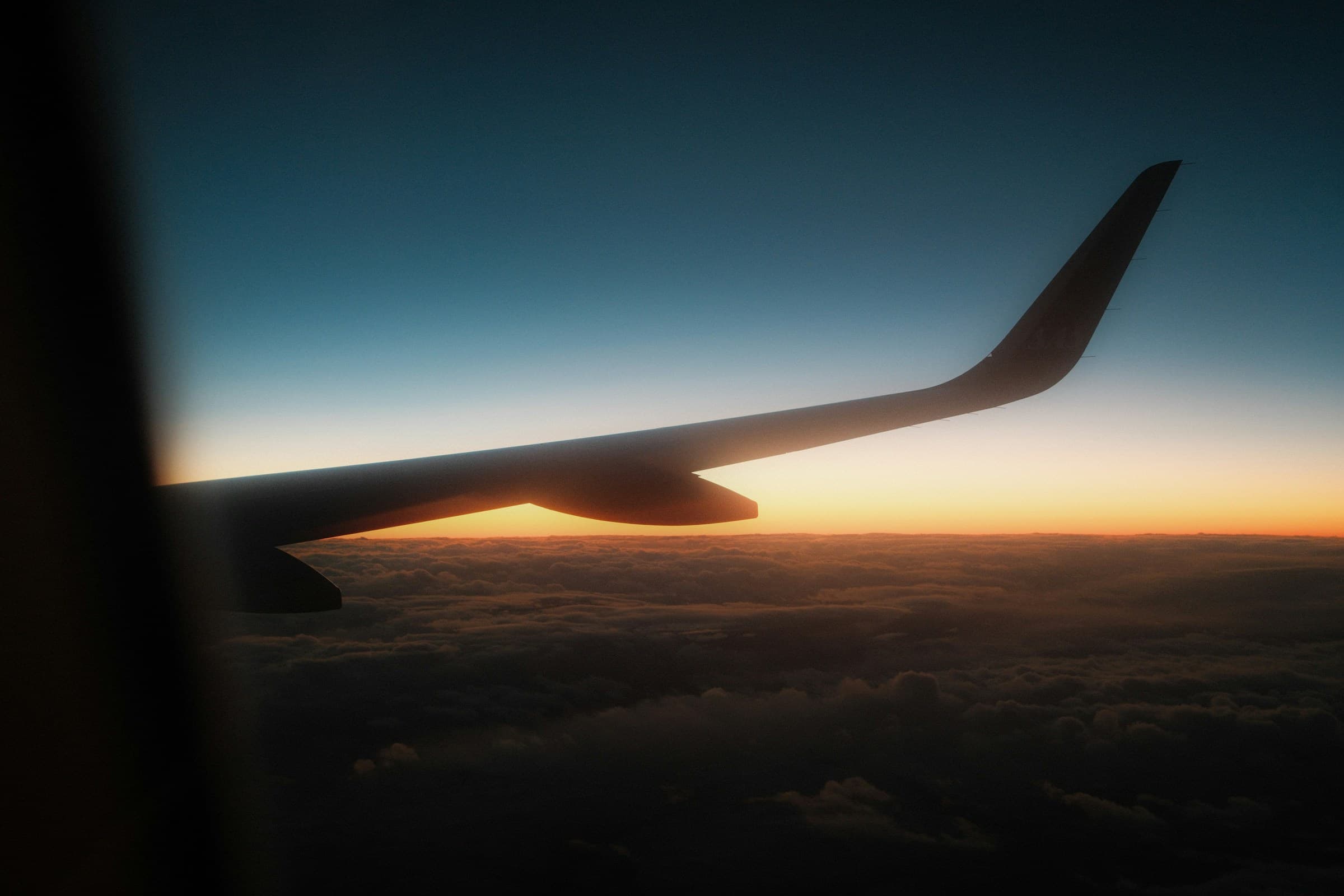 View from an aircraft window of a wing above the clouds at sunset